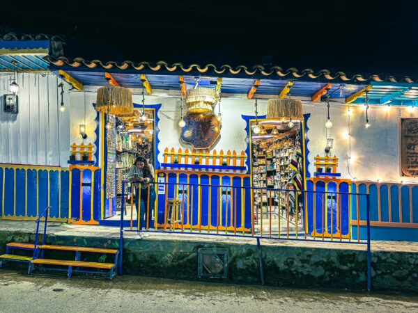 Calle Real features a vibrant, colorful storefront in Salento, Quindio, with blue and orange accents and warm lights creating a welcoming atmosphere.