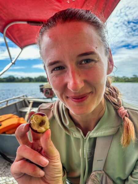 Camu camu fruit held by a smiling woman in a boat at Gamboa Nature Reserve, surrounded by lush greenery in Loreto, Peru.