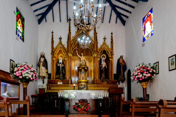 Small church interior at Pueblito Paisa with a gilded altar, statues, chandeliers, and stained-glass windows