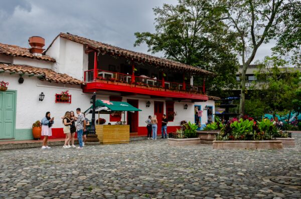 Colorful traditional buildings and lush greenery surround visitors enjoying Pueblito Paisa in Medellín, Antioquia. Cobblestone streets add charm.