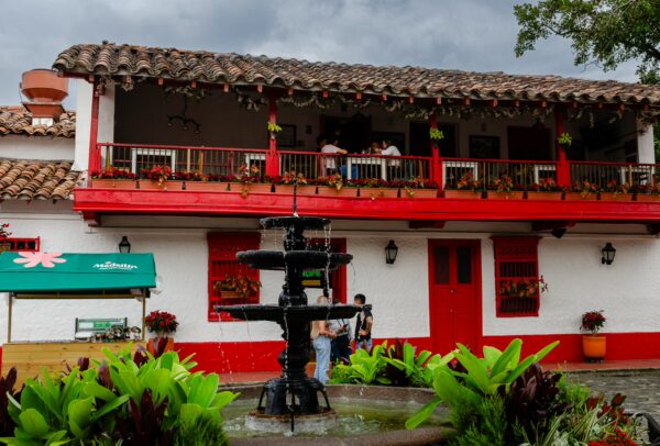 Cobbled plaza at Pueblito Paisa with a central fountain and a white building with red balconies and doors