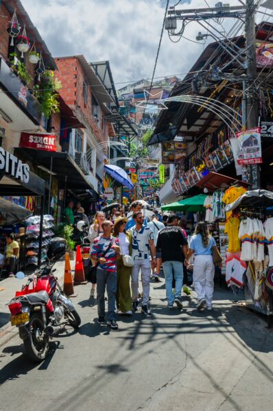 Lively street scene in Comuna 13, Medellín, featuring colorful shops, street vendors, and various visitors enjoying local culture.