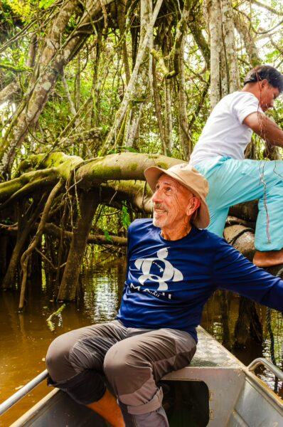 Two men navigate a boat through the lush greenery of Gamboa Nature Reserve in Loreto, Peru, surrounded by dense trees and calm waters.