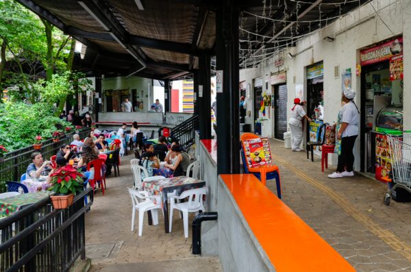 Colorful outdoor dining scene at Pueblito Paisa in Medellín, with visitors enjoying meals amid lush greenery and vibrant vendor stalls.