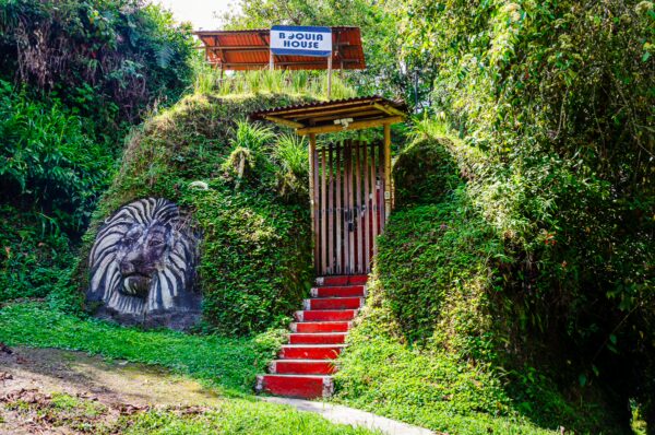 Colorful wooden entrance leads to a garden with lush greenery and a carved lion's head at Salento, Quindío, Colombia.