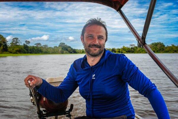 A man smiles while steering a boat on Pirana Lake in Gamboa Nature Reserve, surrounded by lush greenery in Loreto, Peru.