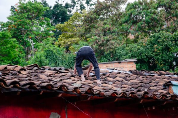 A person in black pants balances on a tiled roof, surrounded by vibrant green trees in Medellin, Antioquia, Colombia.