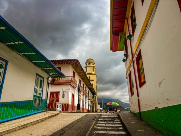 Colorful buildings framing a cobblestone street under a moody sky in Salento, Quindío, Colombia, showcasing local architecture.
