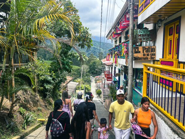Colorful houses line the hillside in Salento, Quindío, with locals walking along a winding street surrounded by lush greenery.