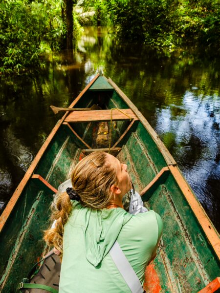 A traveler relaxes in a green canoe on the tranquil waters of Gamboa Nature Reserve, surrounded by lush greenery in Loreto, Peru.