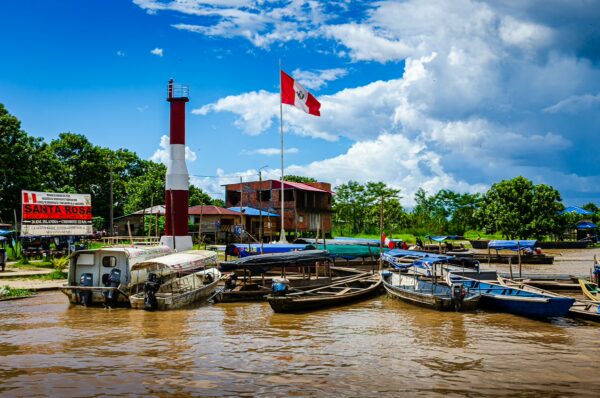 Boats docked by the waterfront in Santa Rosa, Amazonas, Peru, with a vibrant Peruvian flag and lush greenery in the background.