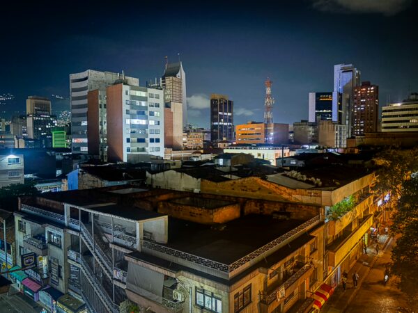 Nighttime skyline of Medellín, Colombia, showcasing illuminated buildings and vibrant city streets beneath a clear sky.