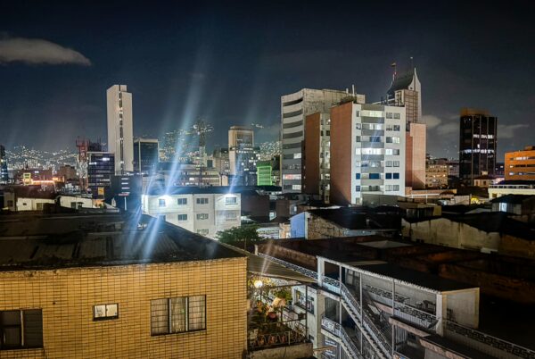 Night view over Medellín’s central skyline, with illuminated buildings and city lights on the hills beyond