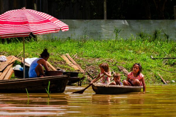 Indigenous community children play in a boat on muddy waters, with a striped red umbrella nearby at Gamboa Nature Reserve, Loreto, Peru.