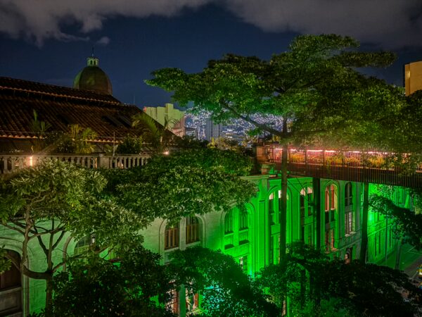 Lush greenery surrounds illuminated buildings in Medellín, Antioquia, with a vibrant city skyline visible in the background.
