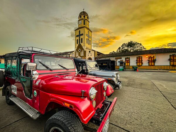 Bright red Willys jeep parked in front of a charming colonial building during sunset in Salento, Quindio, Colombia.