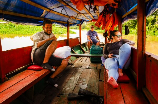 Travelers relax on a wooden boat, surrounded by lush greenery, navigating the Gamboa Nature Reserve in Loreto, Peru.