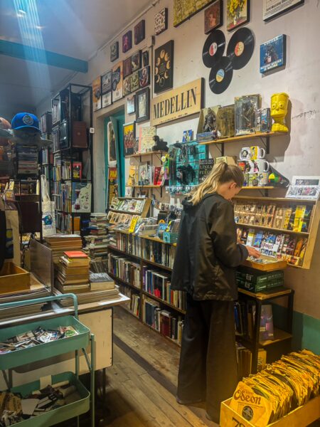 A cozy bookstore in Medellin, Antioquia, filled with colorful books, records, and a visitor browsing through the shelves.