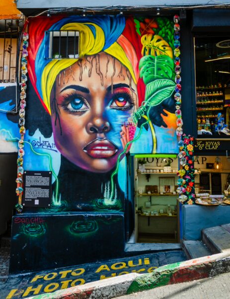 Vibrant mural in Comuna 13, Medellín, showcasing a woman's face with colorful accents and lush green leaves around her.