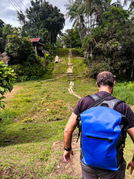 Hiker with a blue backpack travels up a green hill in Puerto Narino, Amazonas, Colombia, surrounded by lush vegetation.