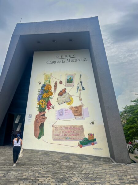 Entrance wall of the Museo Casa de la Memoria in Medellín with a large mural and a person walking up the paved approach
