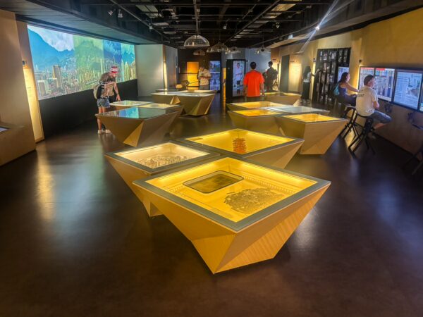 Memory House Museum exhibition room in Medellín with illuminated display tables, wall panels, and visitors viewing displays
