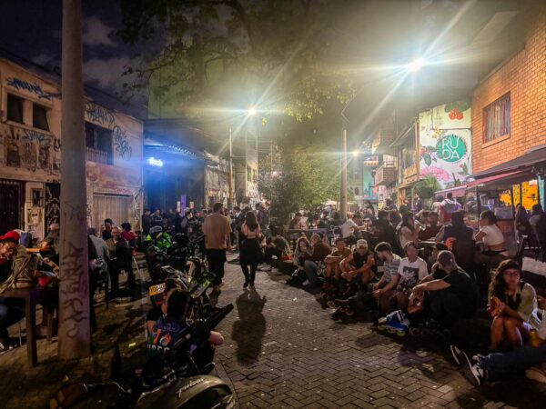 Nighttime on Carrera 42 in Medellín, with crowds gathered outside small bars and street food stalls along a narrow pedestrian street