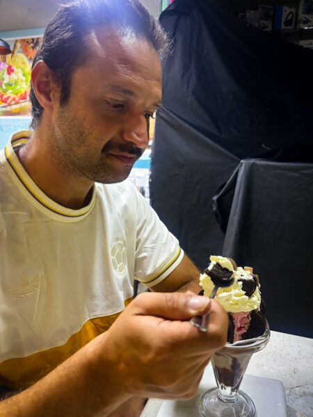 A man enjoys a decadent dessert topped with whipped cream and chocolate, seated at a table in Medellín, Colombia.