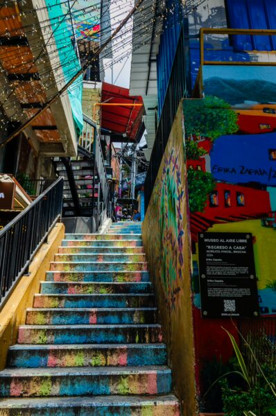 Vibrantly painted stairs lead up through Comuna 13 in Medellín, showcasing colorful murals and lively urban architecture.