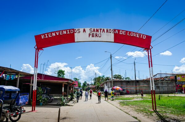 Vibrant welcome archway reading "Bienvenidos a Santa Rosa de Loreto, Peru" amidst a sunny street with people walking.