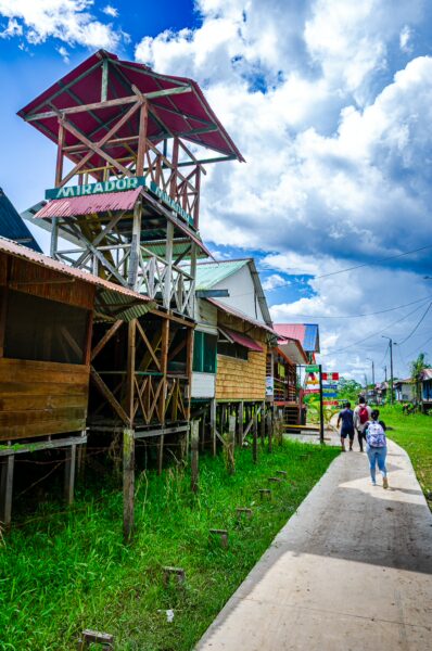 Colorful wooden structures line the pathway in Santa Rosa, Amazonas, Peru, under a bright blue sky with scattered clouds.