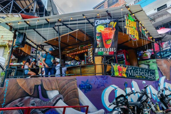 Vibrant bar in Comuna 13, Medellín, featuring colorful murals and patrons enjoying drinks on a lively street.