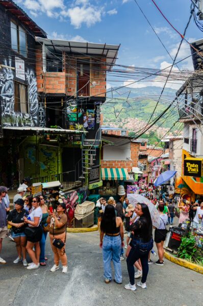 Vibrant street scene in Comuna 13, Medellín, featuring colorful murals, bustling markets, and diverse crowds on a sunny day.