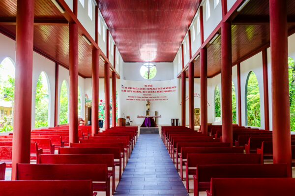Brightly colored interior of a church in Puerto Narino, Amazonas, Colombia, featuring red pews, tall windows, and wooden beams.
