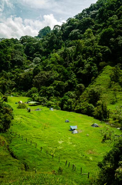 Lush green landscape with rolling hills and tents scattered across the field near Santa Rita Waterfalls in Salento, Quindío, Colombia.