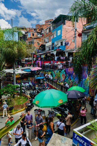 Vibrant street scene in Comuna 13, Medellín, featuring colorful murals, bustling markets, and lush palm trees.