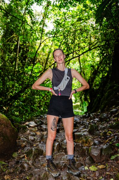 Hiker in a black outfit stands on rocky path surrounded by lush greenery near Santa Rita Waterfalls in Salento, Quindio, Colombia.