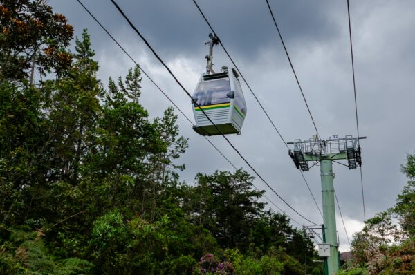 A cable car glides through the lush greenery of Arvi Park in Medellín, Colombia, under a dramatic cloudy sky.