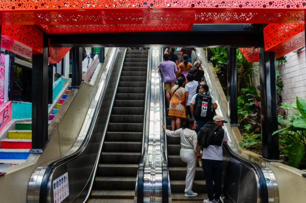 Vibrant escalators in Comuna 13, Medellín, lined with colorful murals and lush plants, bustling with visitors exploring the area.