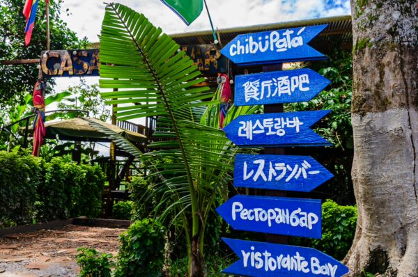 Colorful directional signs guide visitors near the entrance to Chibu-Pata in Puerto Nariño, Amazonas, Colombia. Green foliage enhances the vibrant scene.