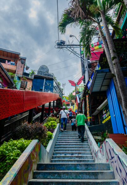 Colorful murals line the stairs and buildings of Comuna 13 in Medellín, Colombia, where visitors explore vibrant street art.