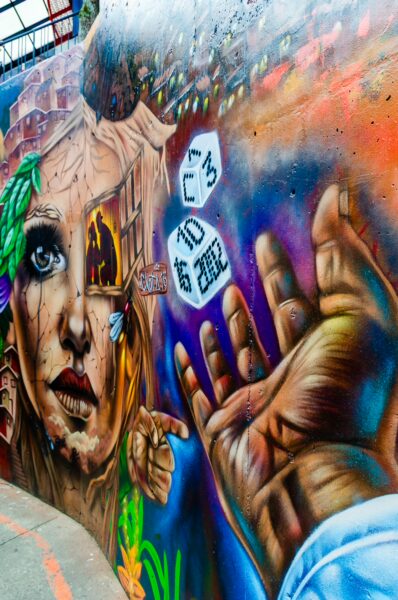 Vibrant mural in Comuna 13, Medellín, showcasing a woman's face and a reaching hand amidst colorful graffiti details.