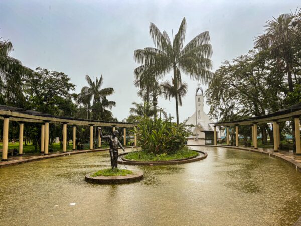 Serene Parque Santander features lush palm trees and a central statue, with a glimpse of a white church in Leticia, Amazonas, Colombia.