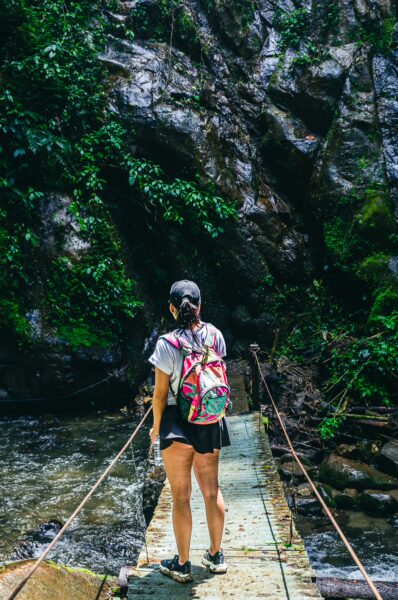 Hiker with a backpack standing on a wooden bridge surrounded by lush greenery near Santa Rita Waterfalls in Salento, Quindio.