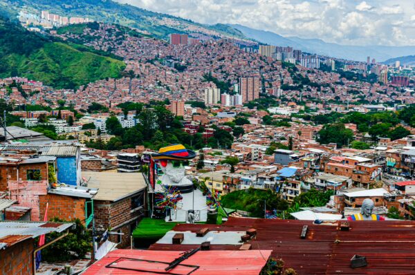 Colorful rooftops cascade down the hillside of Comuna 13 in Medellín, showcasing vibrant community art against a backdrop of lush mountains.