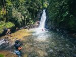 Santa Rita Waterfalls cascades into a clear pool, surrounded by lush greenery and visitors enjoying the refreshing waters in Salento, Quindío.