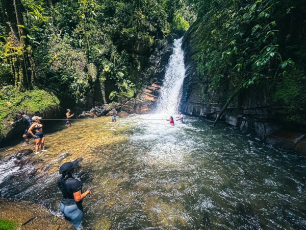 Santa Rita Waterfalls cascades into a clear pool, surrounded by lush greenery and visitors enjoying the refreshing waters in Salento, Quindío.