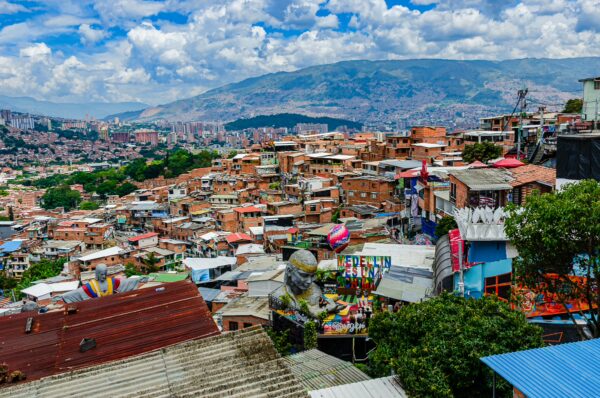 Vibrant rooftops of Comuna 13 in Medellín, Colombia, with colorful murals and the backdrop of lush mountains under a blue sky.