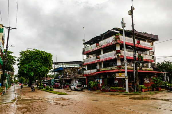 Bustling street scene in Leticia, Amazonas, Colombia, featuring rainy weather, local buildings, and lush green trees.