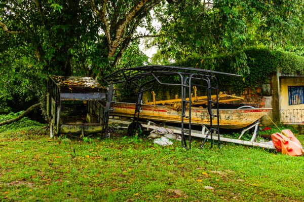 Colorful boats resting on a grassy area under lush trees in Leticia, Amazonas, Colombia, with rustic structures nearby.
